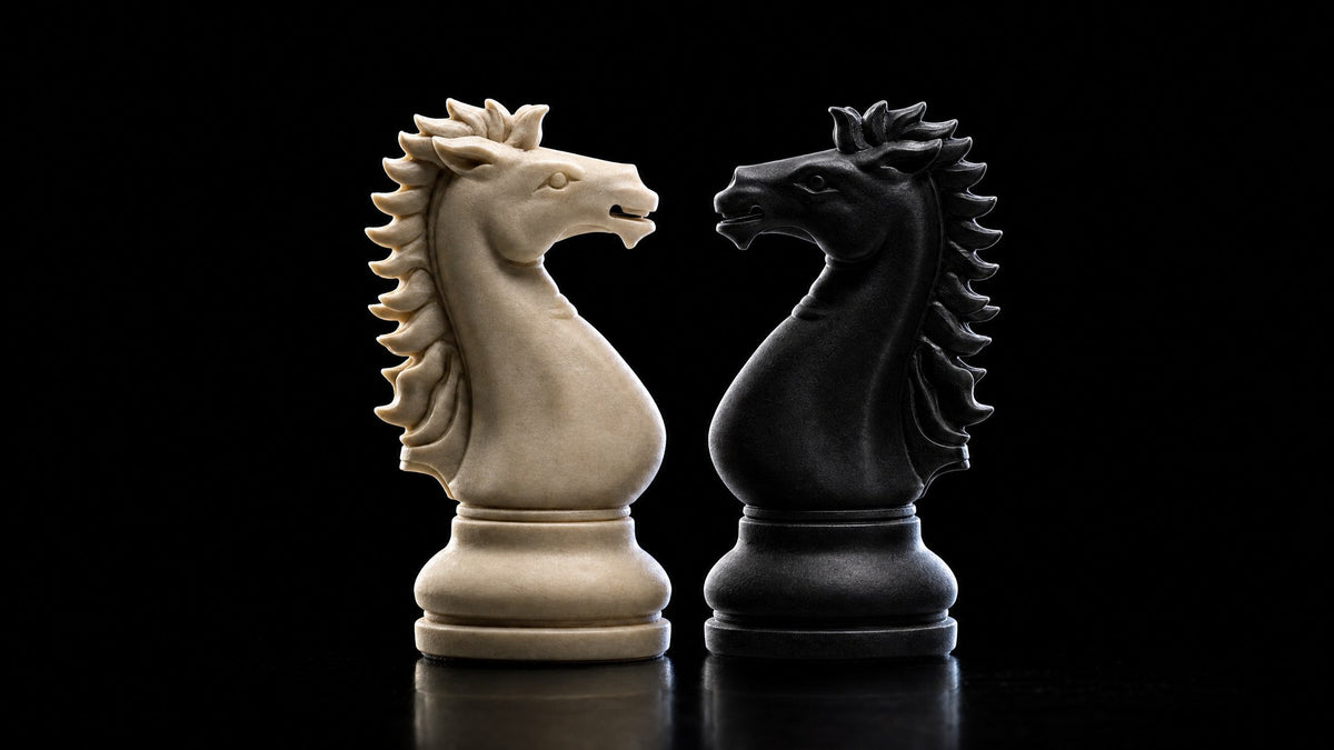 A cream knight and a black knight facing each other nose to nose in dramatic side light