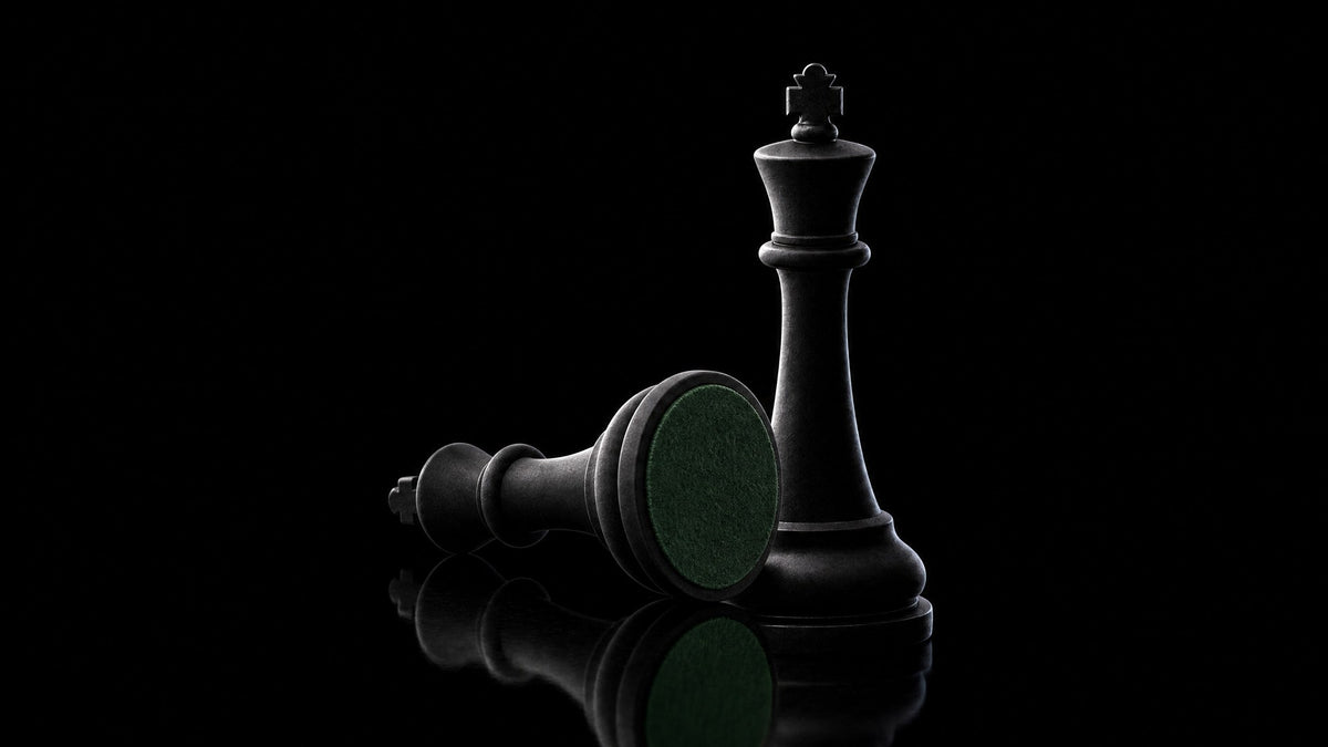 A black chess king lying on its side showing its weighted felt base, with a second king standing behind it